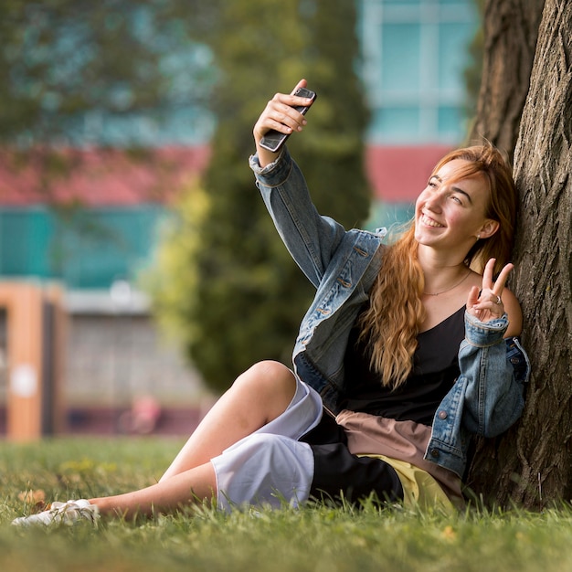 Mulher sentada ao lado de uma árvore tirando uma selfie