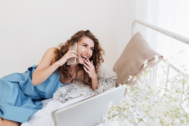 Mulher sentada dentro de casa na cama, falando por telefone. olhando de lado.