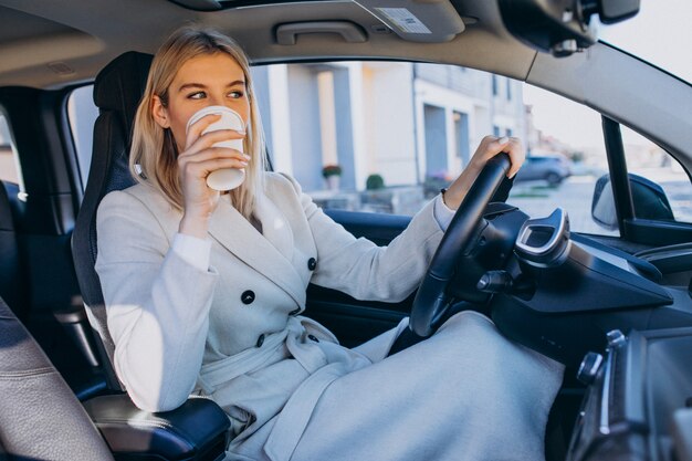 Mulher sentada dentro do carro elétrico enquanto carregava com uma xícara de café