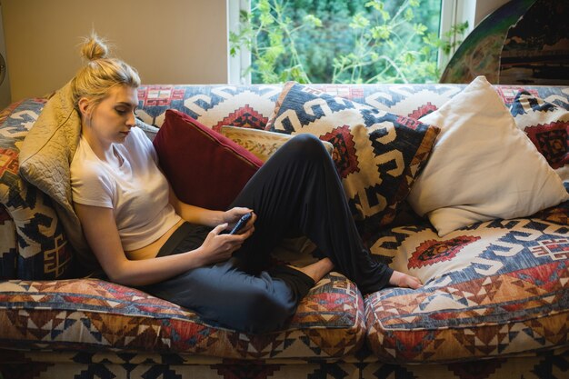Mulher sentada e usando o celular no sofá da sala
