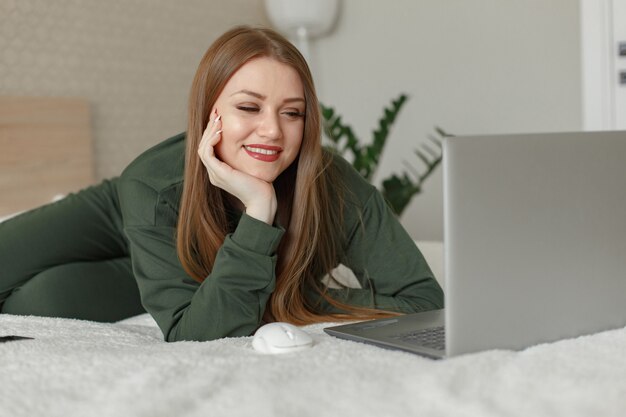 Mulher sentada em uma cama e usa um laptop