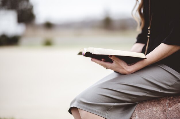 Mulher sentada em uma rocha ao ar livre enquanto lê um livro
