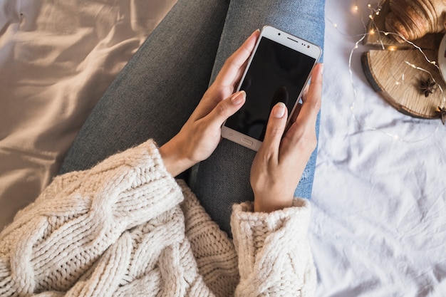 Mulher sentada na cama e usando smartphone