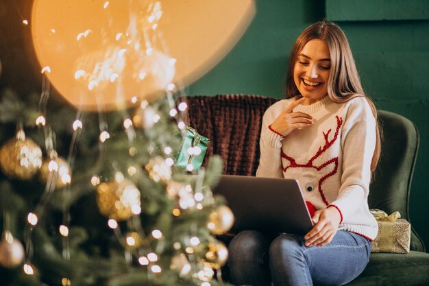 Mulher sentada perto da árvore de Natal e compras de vendas on-line