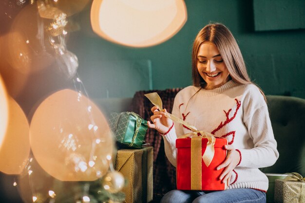 Mulher sentada perto da árvore de Natal e desembalar o presente de Natal