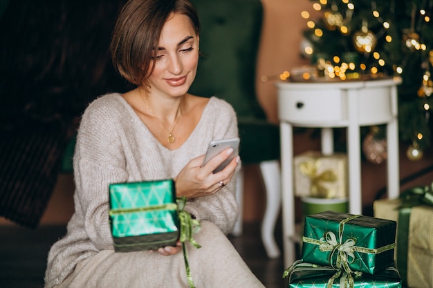 Mulher sentada perto da árvore de natal e fazer compras no telefone