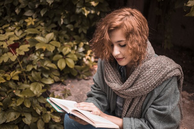 Mulher, sentando, bordo, e, atentamente, livro leitura, perto, planta