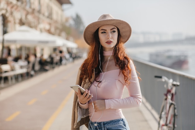 Mulher séria com cabelo ruivo ondulado esperando amigo no aterro