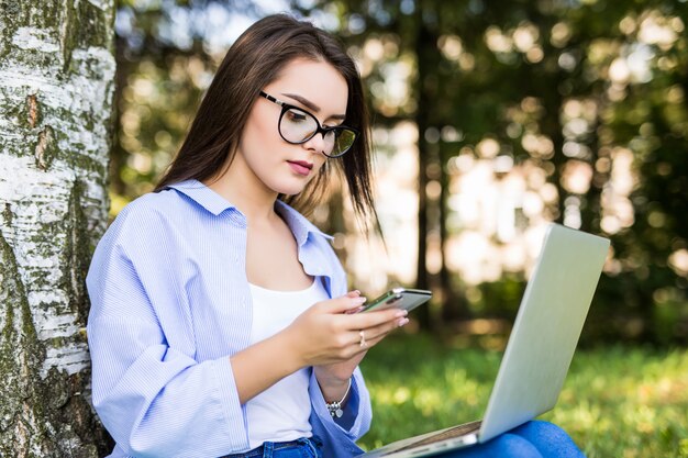 Mulher séria em jeans trabalhando com laptop no parque da cidade