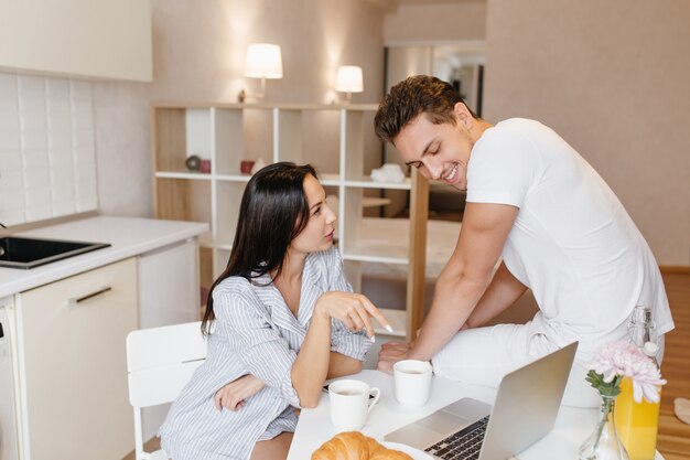 Mulher séria usando camisa masculina como pijama conversando com o namorado na cozinha