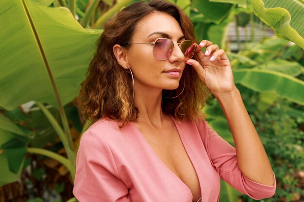 Mulher sexy europeu com cabelos encaracolados no vestido rosa em cima de palmeiras.