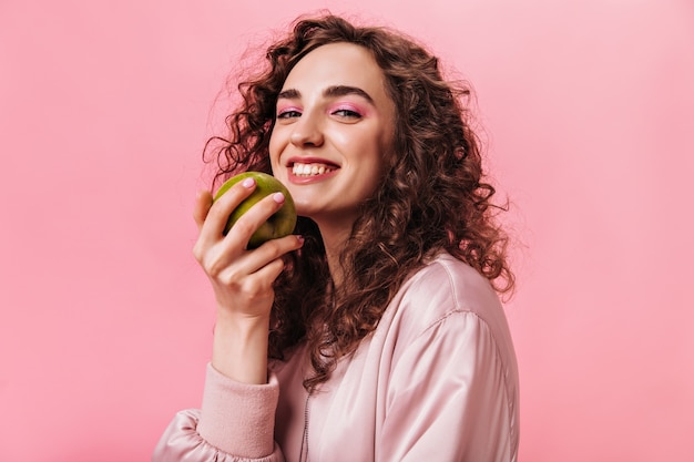 Mulher simpática de bom humor segurando uma maçã verde sobre fundo rosa