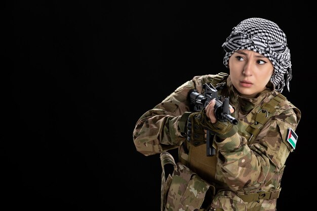 Mulher soldado em uniforme militar mirando metralhadora na parede preta