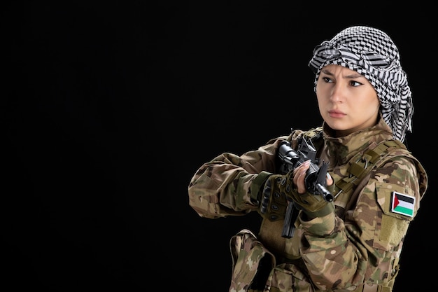 Mulher soldado em uniforme militar mirando metralhadora na parede preta