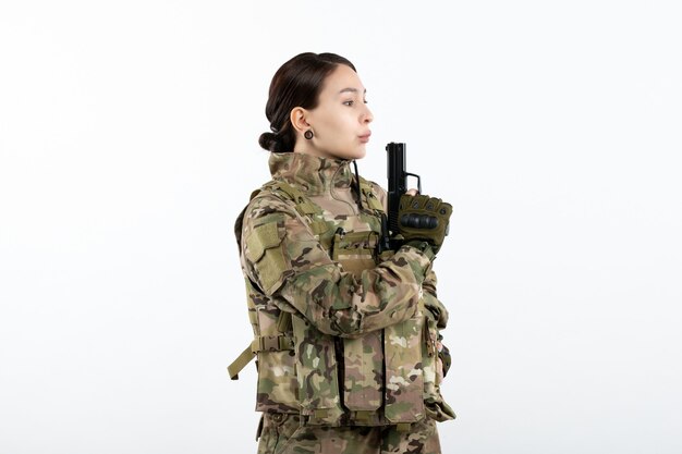 Mulher soldado frontal camuflada com arma na parede branca