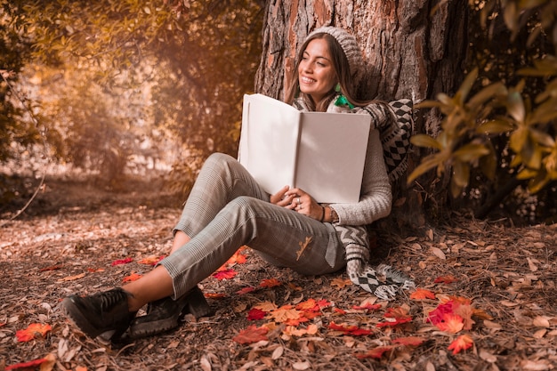 Mulher sonhadora com livro sentado perto da árvore