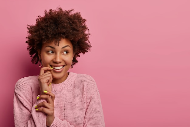 Mulher sonhadora positiva olha para o lado, tem sorriso terno, dentes brancos