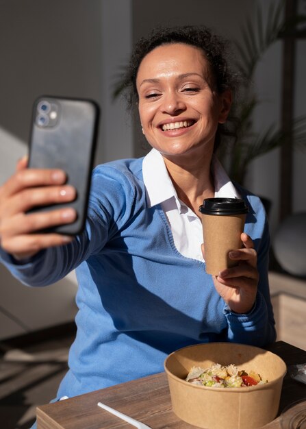 Mulher sorridente a comer comida para levar e a tirar uma selfie