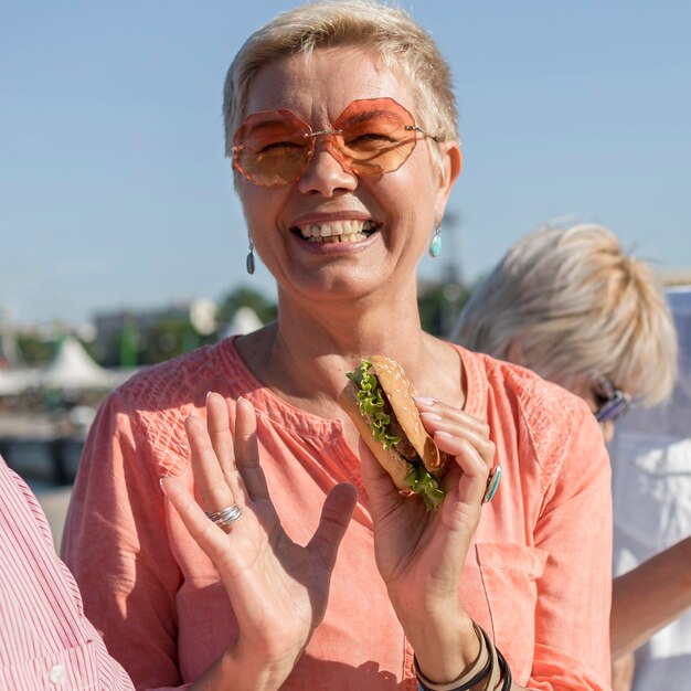 Mulher sorridente a comer um hambúrguer ao ar livre