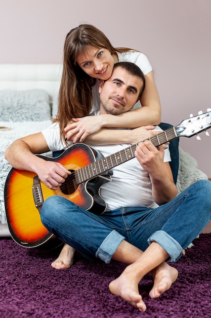 Mulher sorridente, abraçando o namorado tocando violão