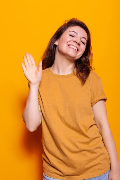 Mulher sorridente acenando com a palma da mão para a câmera no estúdio, se divertindo. Pessoa alegre fazendo gesto de saudação para cumprimentar as pessoas e acenando com a mão. Jovem adulto sendo amigável, fazendo símbolo de saudação