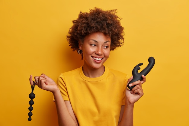 Foto grátis mulher sorridente alegre e feliz por voltar do sex shop, segurando contas anais que estimulam o movimento do ânus, vibrador para chegar ao clímax, estar de bom humor, não posso esperar até a masturbação