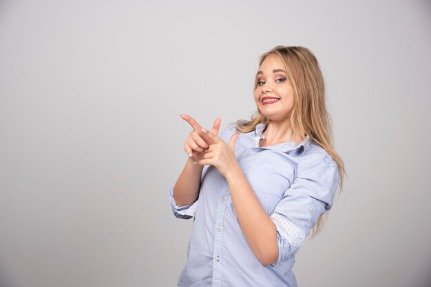 Mulher sorridente apontando para algum lugar na superfície cinza