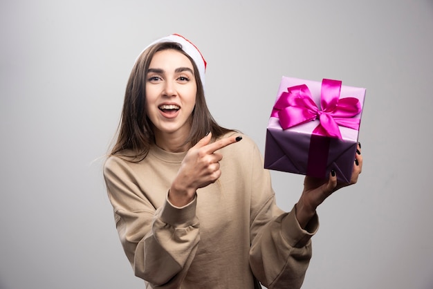 Mulher sorridente, apontando para uma caixa de presente de natal.