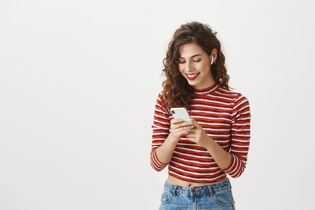 Mulher sorridente assistindo vídeo no celular usando fones de ouvido sem fio