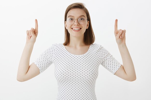 Mulher sorridente atraente apontando o dedo para cima, mostrando o anúncio