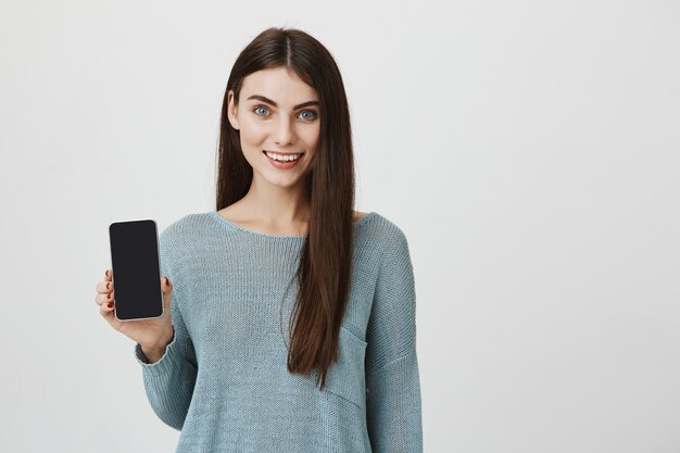 Mulher sorridente atraente promove aplicativo, mostra tela de smartphone