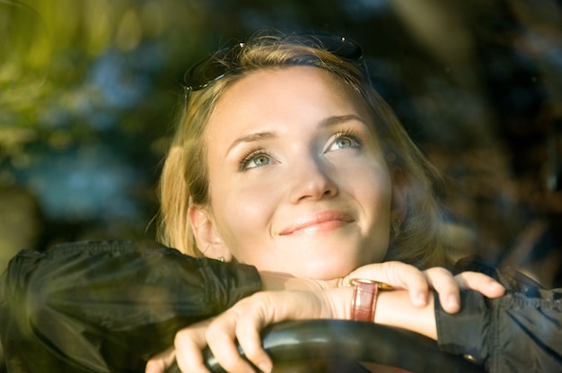 Mulher sorridente atraente sonha no carro novo e olhando para cima - ao ar livre