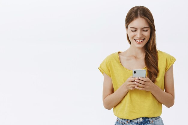 Mulher sorridente atraente usando telefone celular, mensagem de texto no aplicativo ou rede social