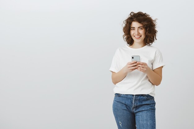 Mulher sorridente atraente usando telefone celular, mensagens de texto, mídia social de rolagem