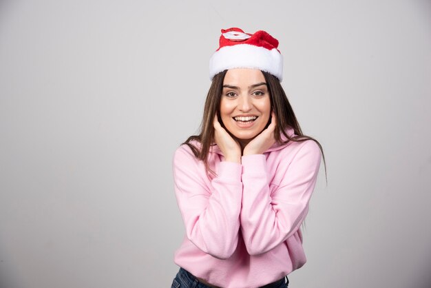 Mulher sorridente com chapéu de Papai Noel vermelho, corrigindo o cabelo.