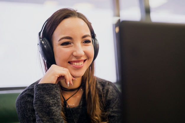 Mulher sorridente com fones de ouvido na cabeça olhando para laptop