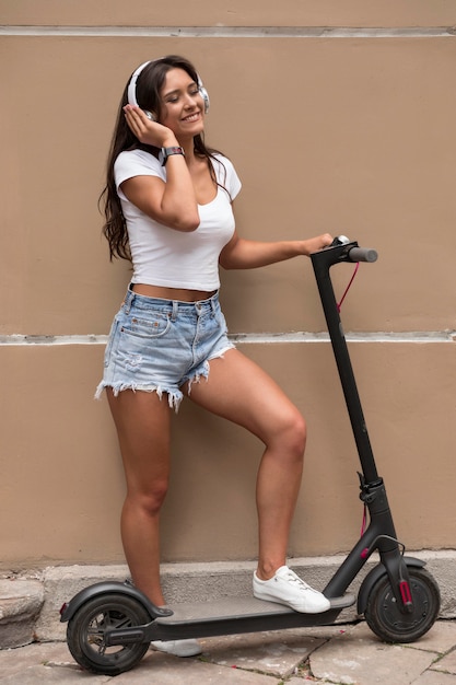 Mulher sorridente com fones de ouvido posando ao lado de uma scooter elétrica