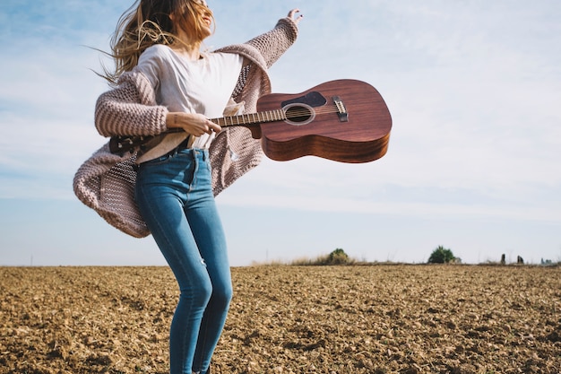 Mulher sorridente com guitarra pulando no campo