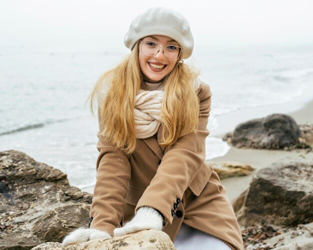 Mulher sorridente com luvas na praia durante o inverno