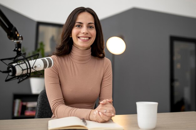 Mulher sorridente com microfone e café em um estúdio de rádio