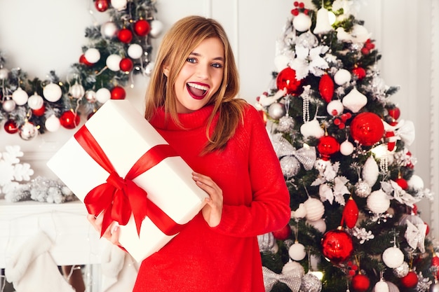 Mulher sorridente com muitas caixas de presente se passando perto da árvore de Natal decorada