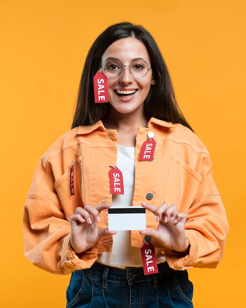 Mulher sorridente com óculos segurando um cartão de crédito enquanto é coberta por etiquetas de venda