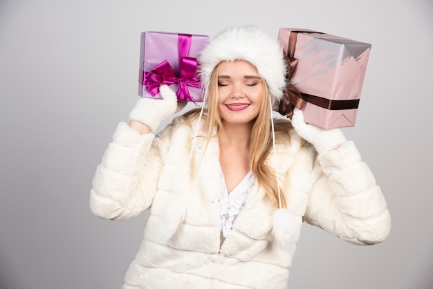 Mulher sorridente com roupa de inverno, segurando caixas de presente.
