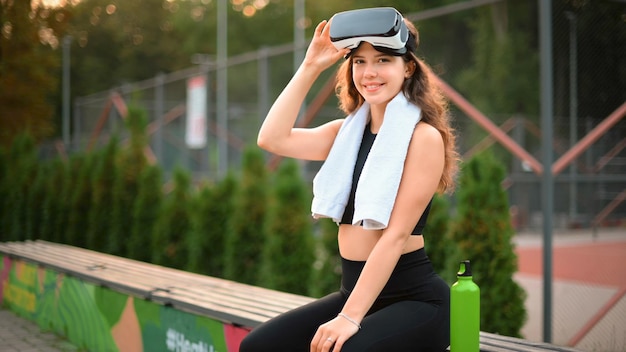 Foto grátis mulher sorridente com toalha de fone de ouvido vr e garrafa de água em um agasalho olhando para a câmera