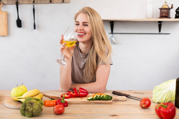 Mulher sorridente com um copo e legumes na cozinha