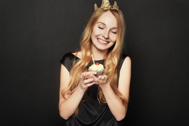 Mulher sorridente, com uma coroa, segurando um bolo de aniversário