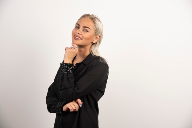 Mulher sorridente de camisa preta, posando em fundo branco. Foto de alta qualidade