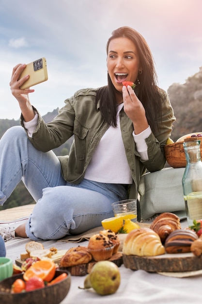 Mulher sorridente de tiro completo tomando selfie enquanto come