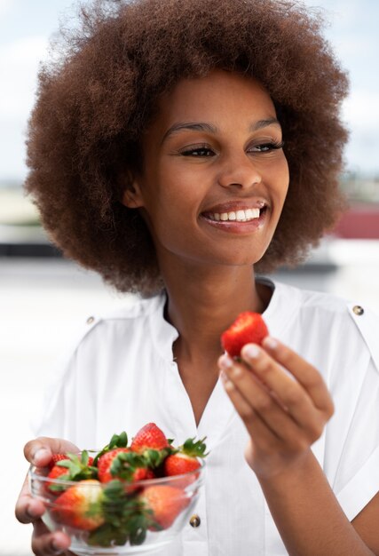 Mulher sorridente de tiro médio comendo morangos