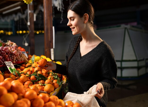 Mulher sorridente de tiro médio comprando tangerina